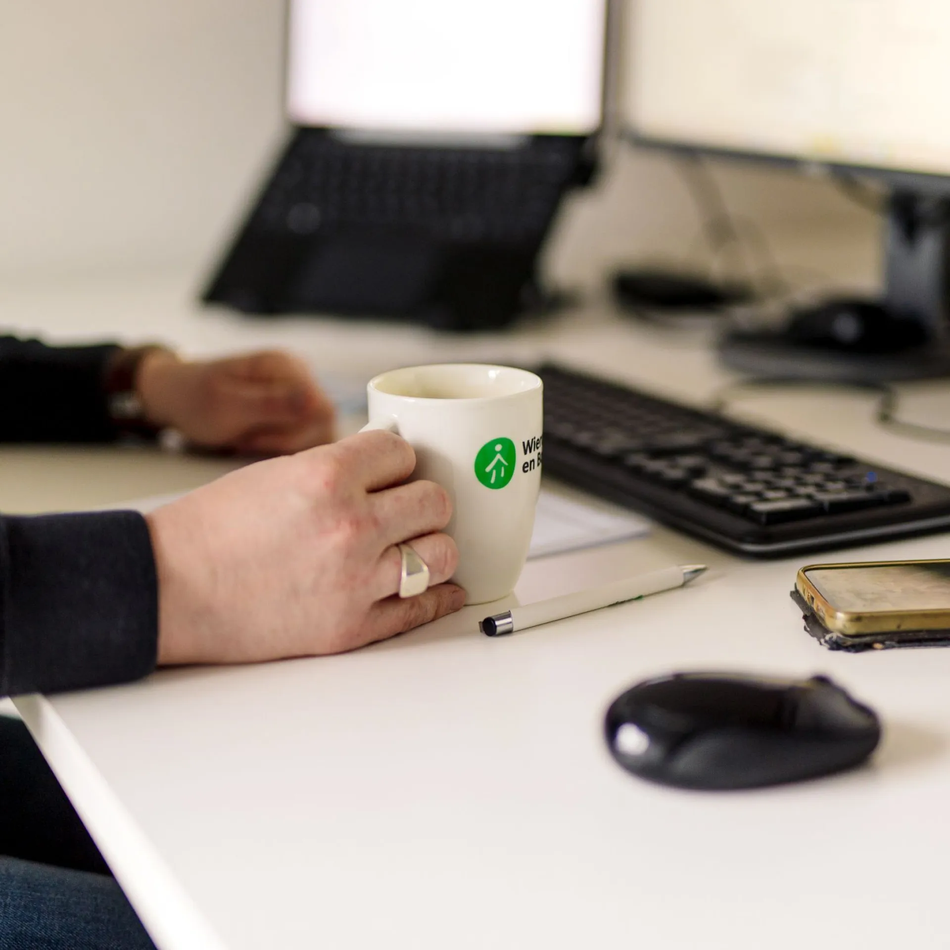 Kop koffie in de hand aan een bureau